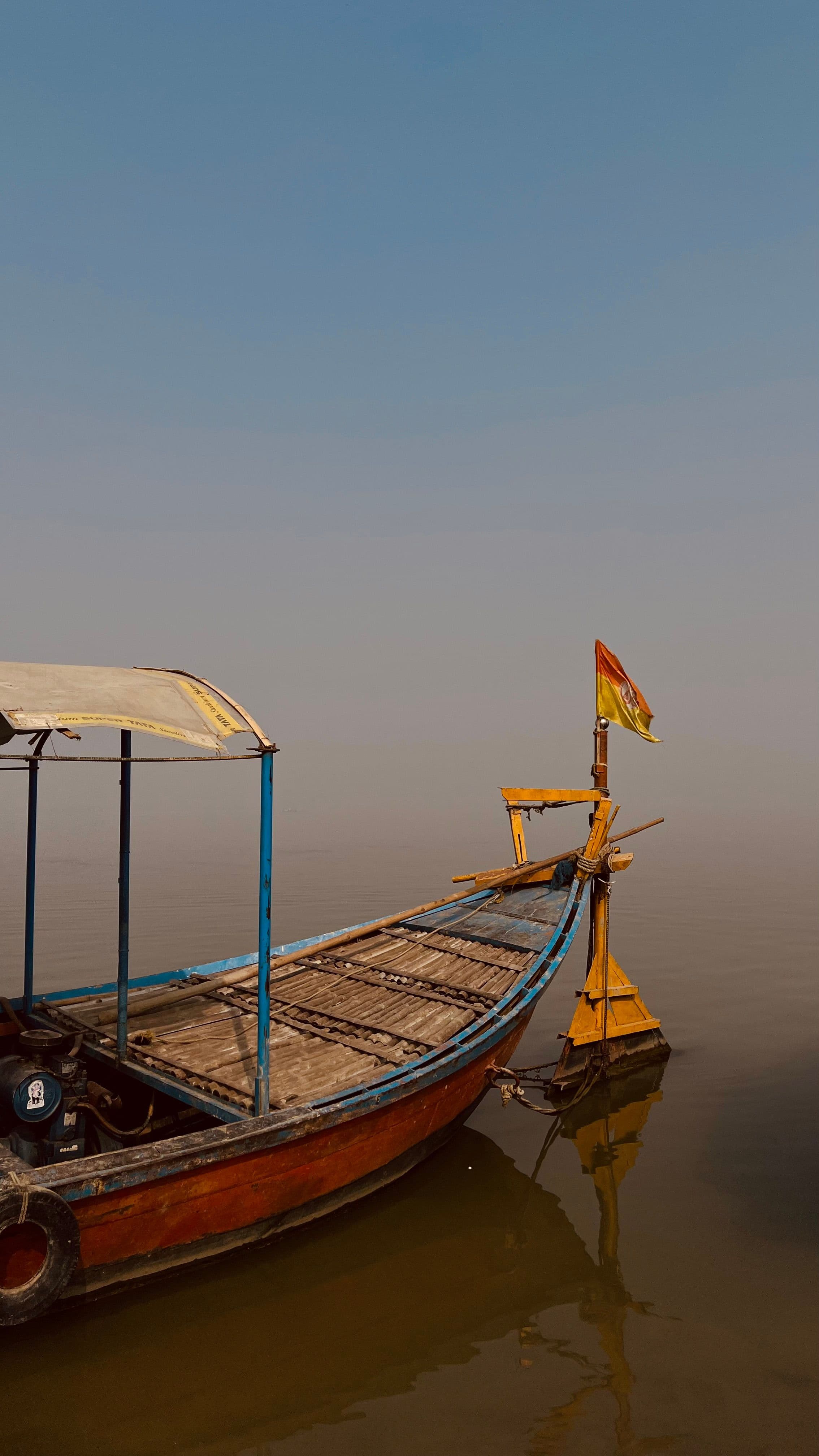 A wooden boat with a saffron flag moored on a still, misty Yamuna