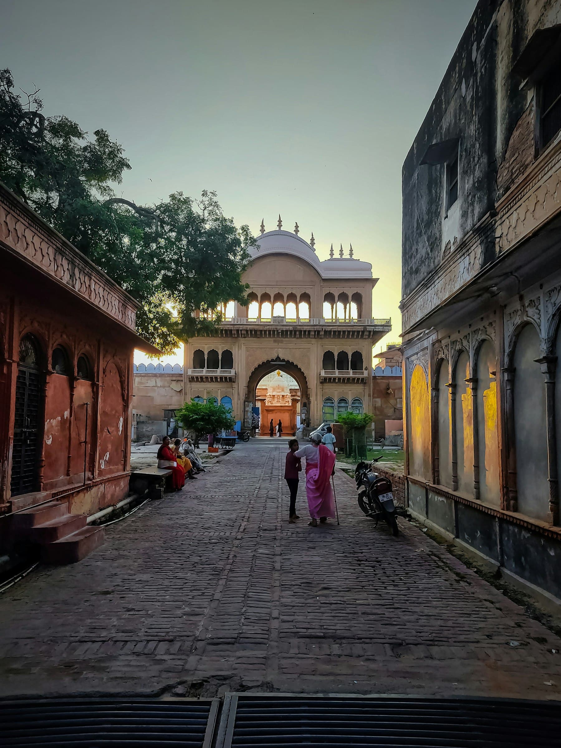 A Vrindavan lane at dusk, people walking beneath an old gateway arch