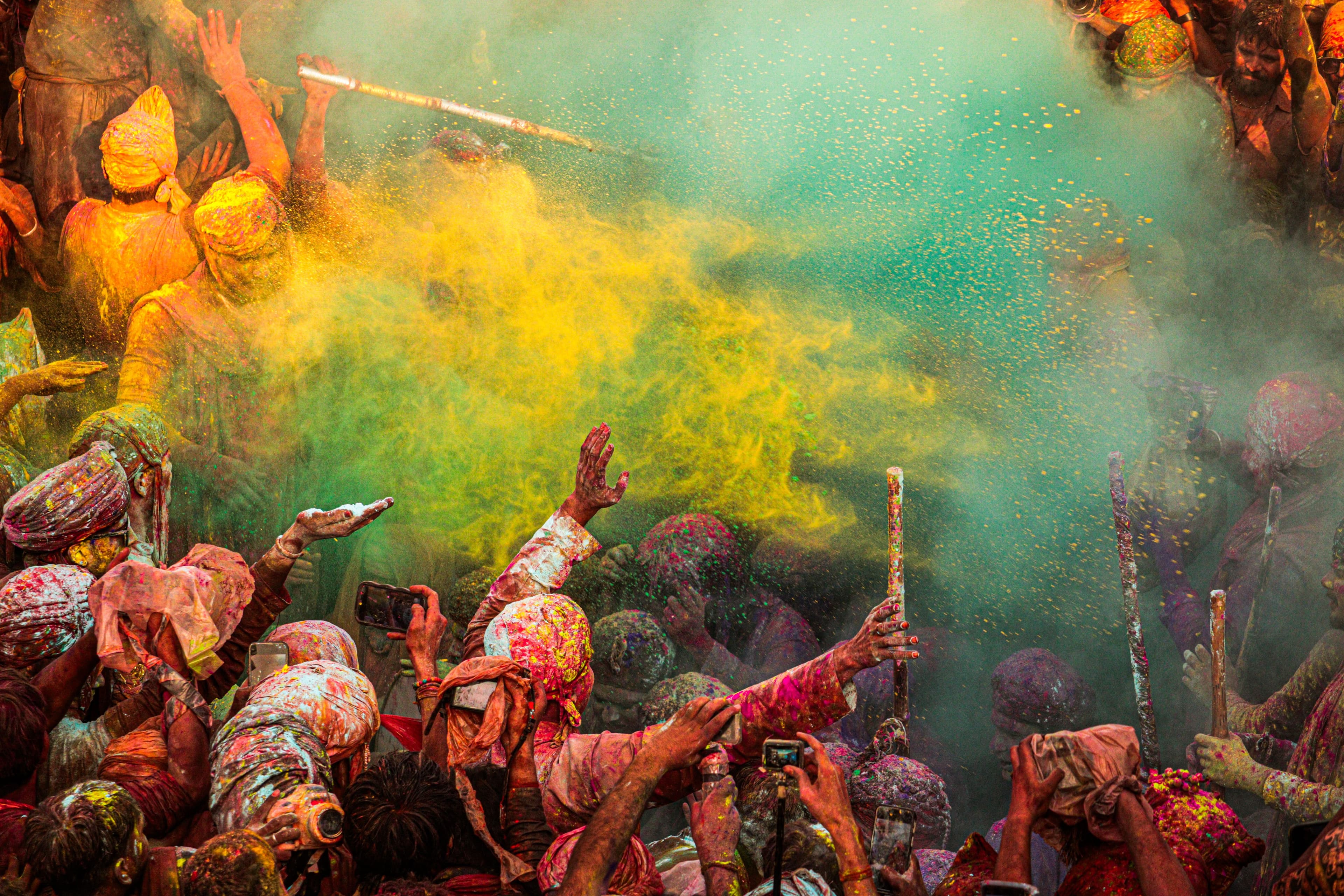 Clouds of yellow and green colour over a dense crowd at Lathmar Holi, lathis raised above the heads