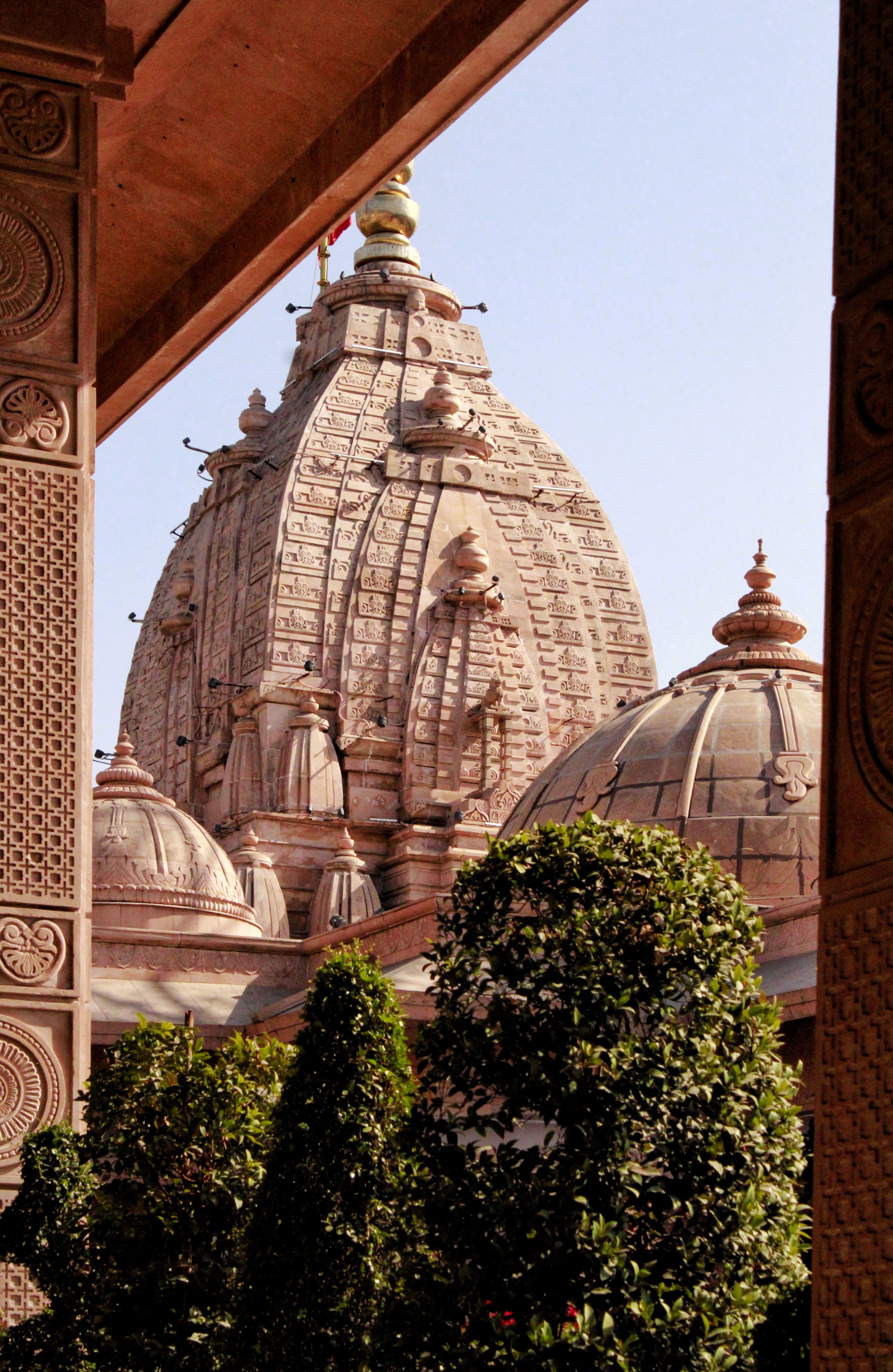 The carved sandstone shikhara at Shri Krishna Janmabhoomi, Mathura, seen through a colonnade