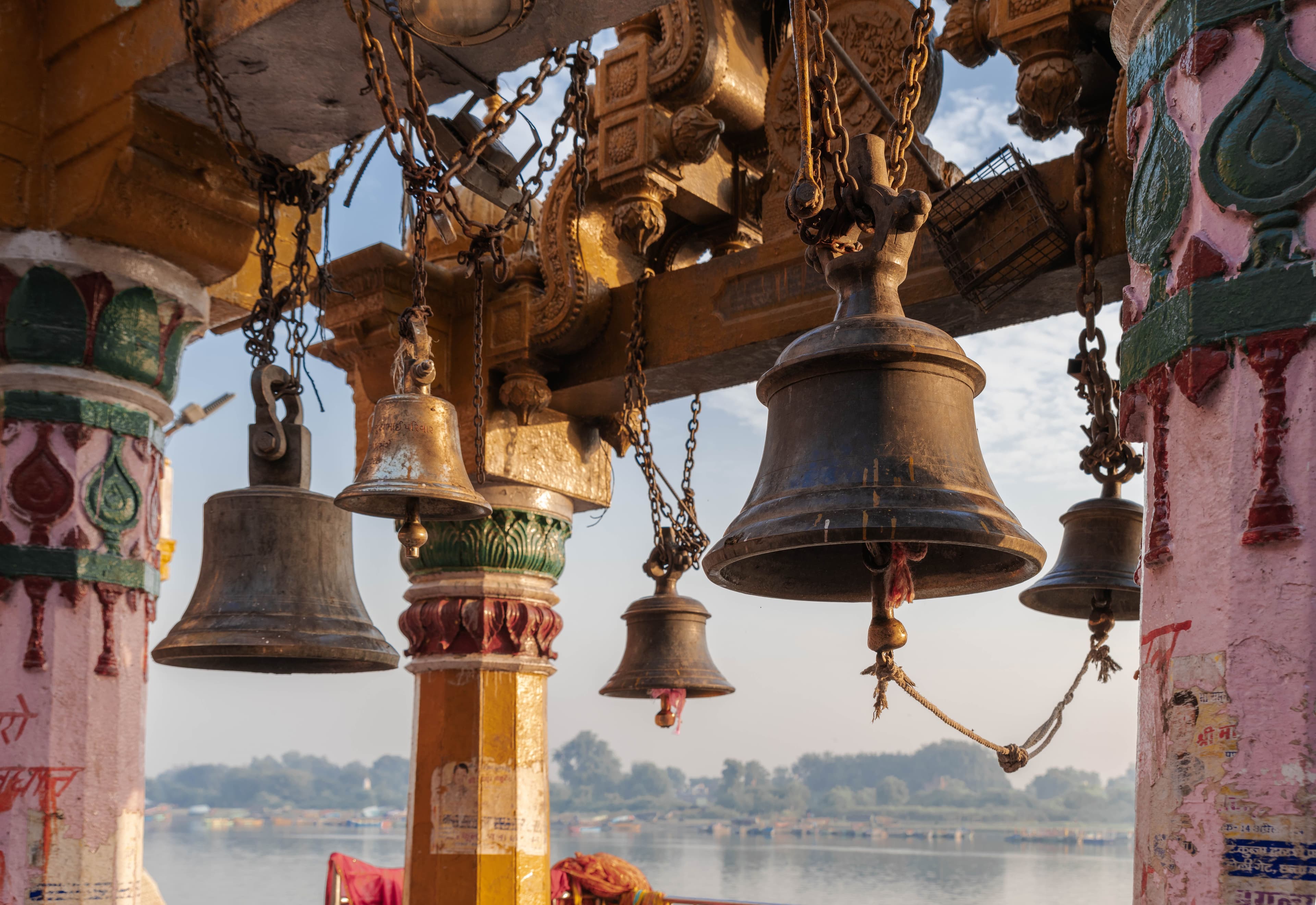 Brass temple bells hanging from painted pillars, the Yamuna visible beyond
