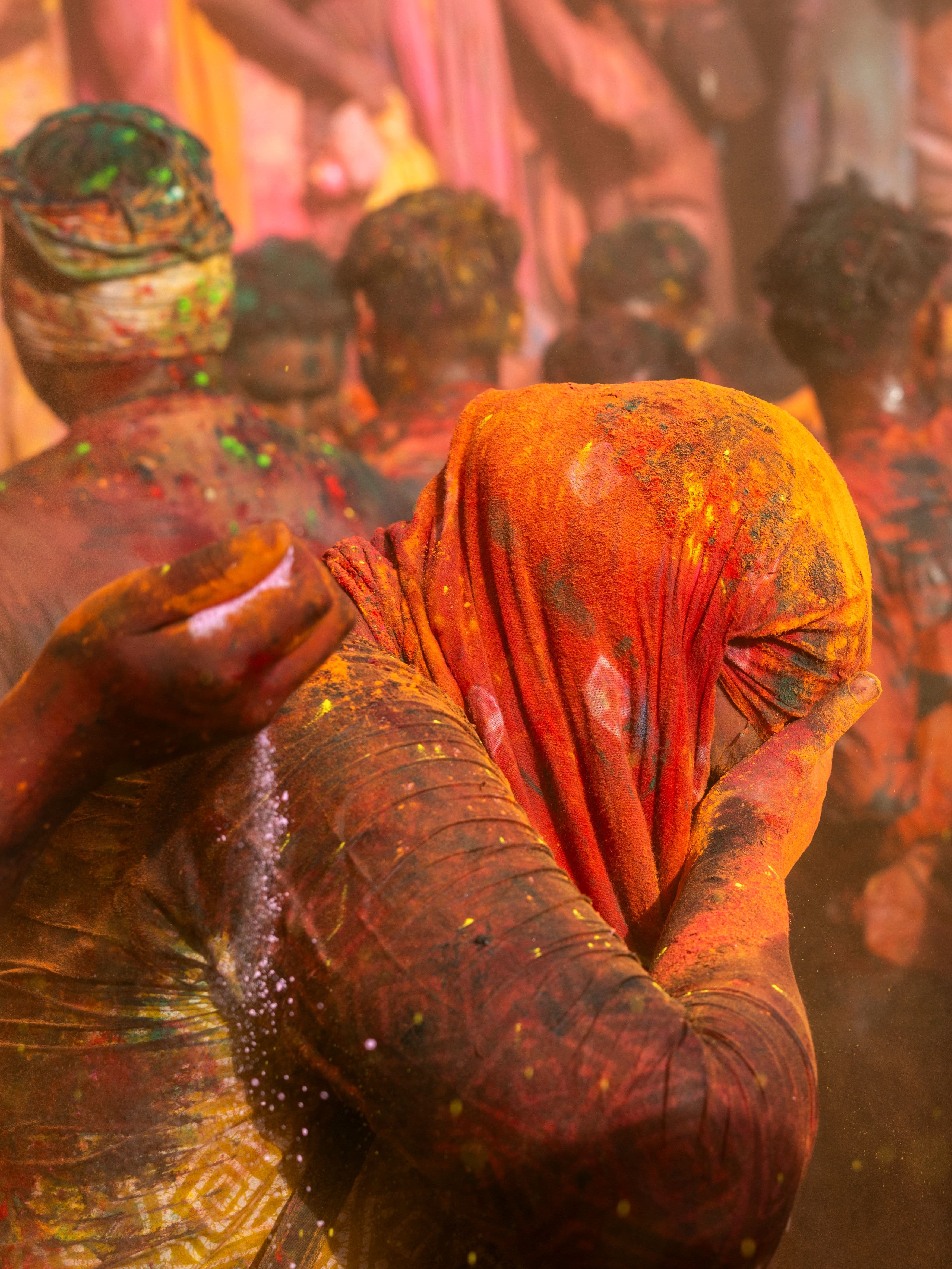 A devotee shielding their face with a colour-drenched chunri in the middle of Holi