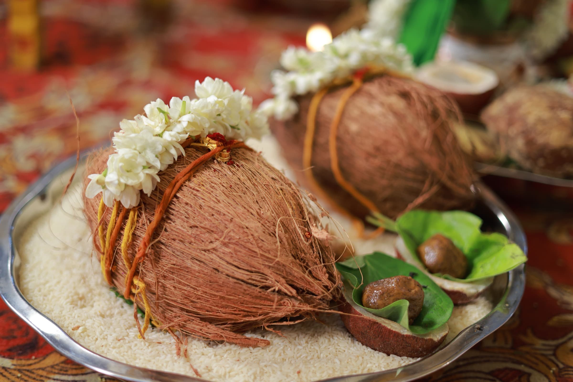 Two garlanded coconuts on a thali of grain, betel leaves and flowers laid out for a puja