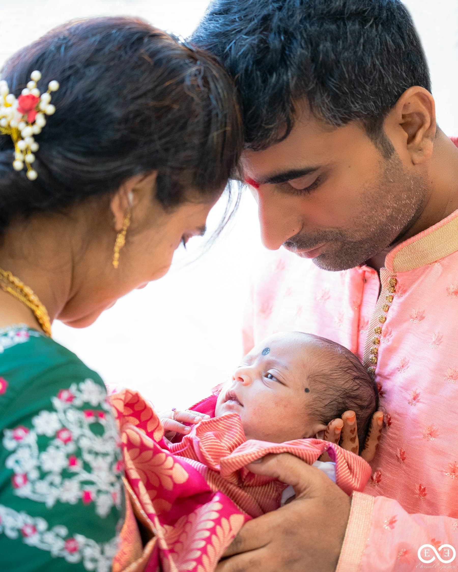 Parents holding a newborn close, the mother dressed for the ceremony