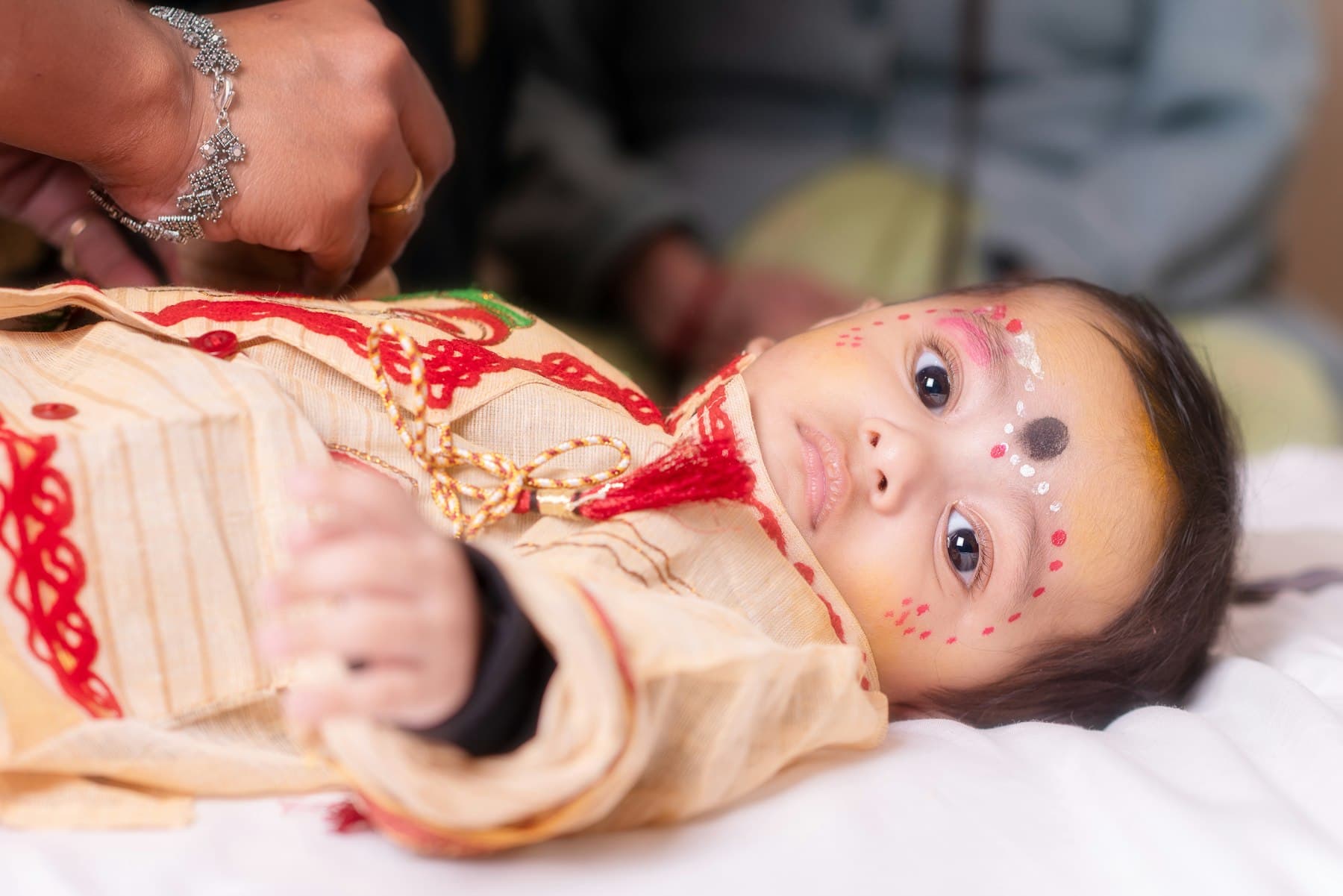 A baby dressed in red and gold for a sanskar, marked with kajal and tilak