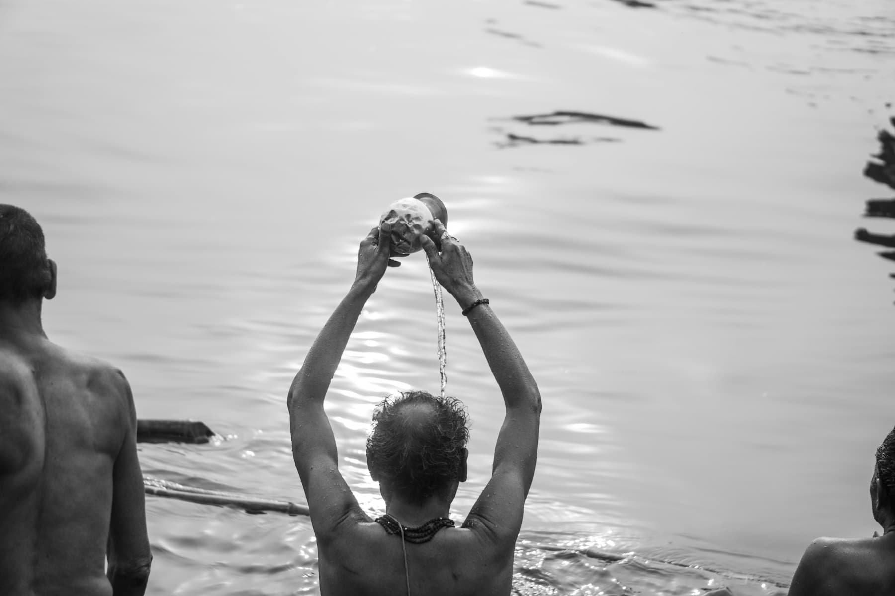 A man standing in the river raising a conch above his head during tarpan