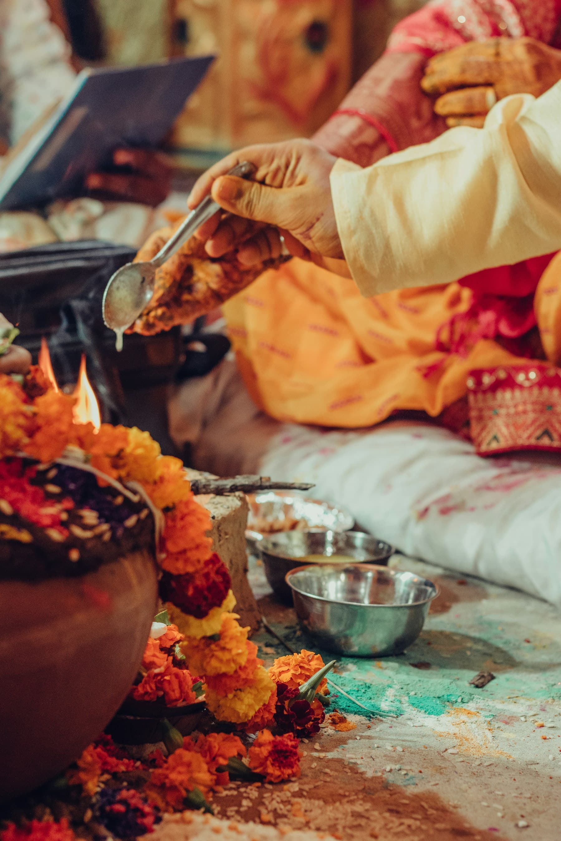 A purohit pouring an offering at a marigold-draped kalash, the family seated alongside