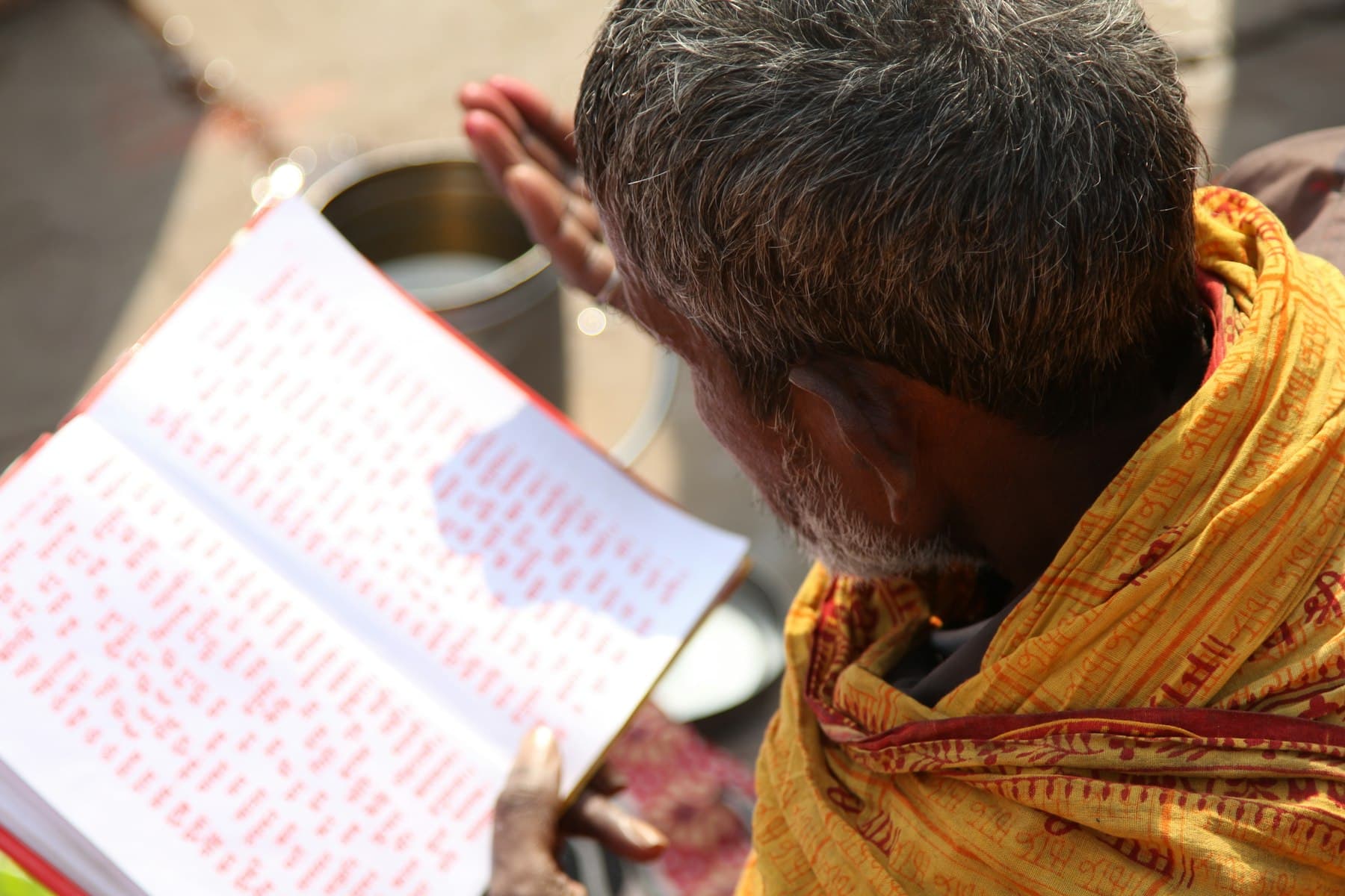 A reader in saffron bent over the loose pages of the text