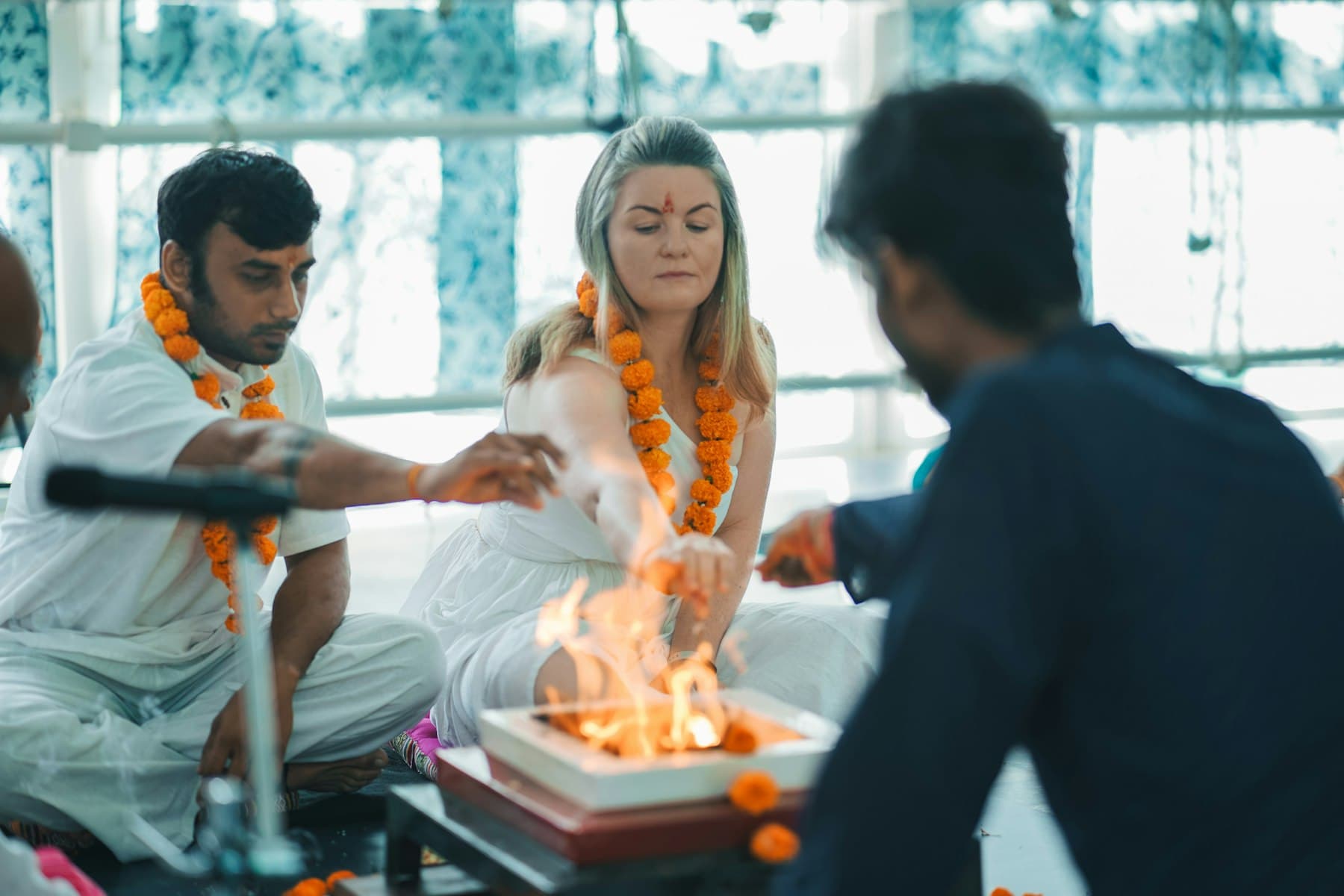 A garlanded couple seated at the havan while the purohit tends the fire