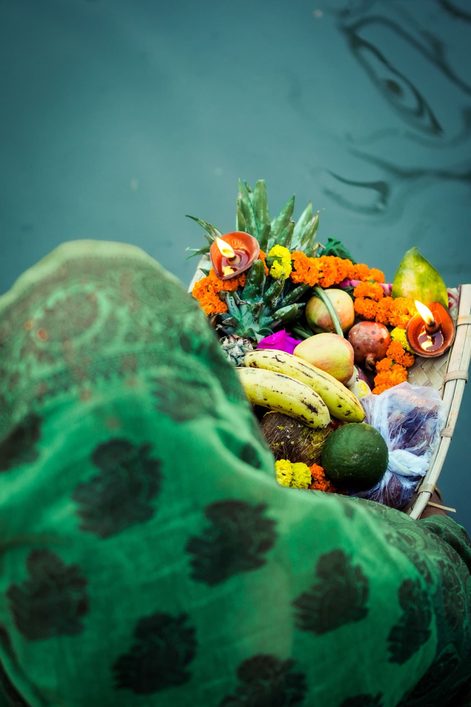 A woman carrying a basket of fruit, marigolds and a lit lamp down to the water for the puja