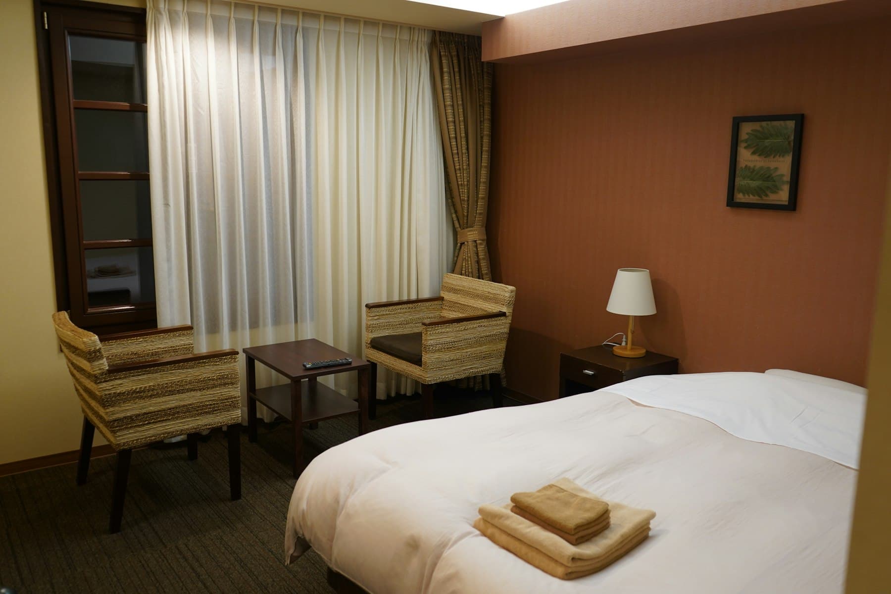 A simple hotel room with a bed and a chair by the window